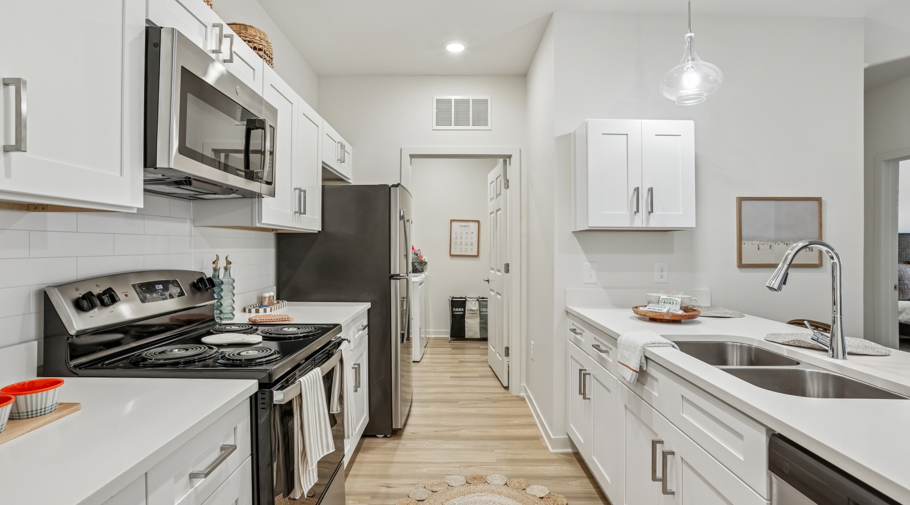 Two Bedroom Apartments In Pensacola, FL - Casara Pensacola - A Kitchen With White Cabinets, Quartz Countertops, Stainless Steel Appliances, Soft Pendant Lighting, And Light Wood Flooring.