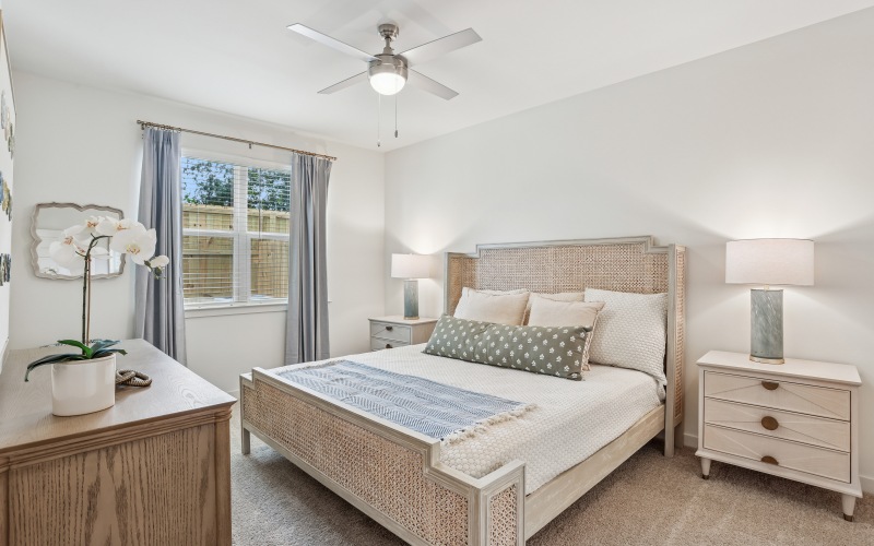 2 Bedroom Apartments In Pensacola, FL - Casara Pensacola - A Bedroom With Woven Furniture, White Bedding, Sleek Ceiling Fan, Matching Lamps, and Large Window.